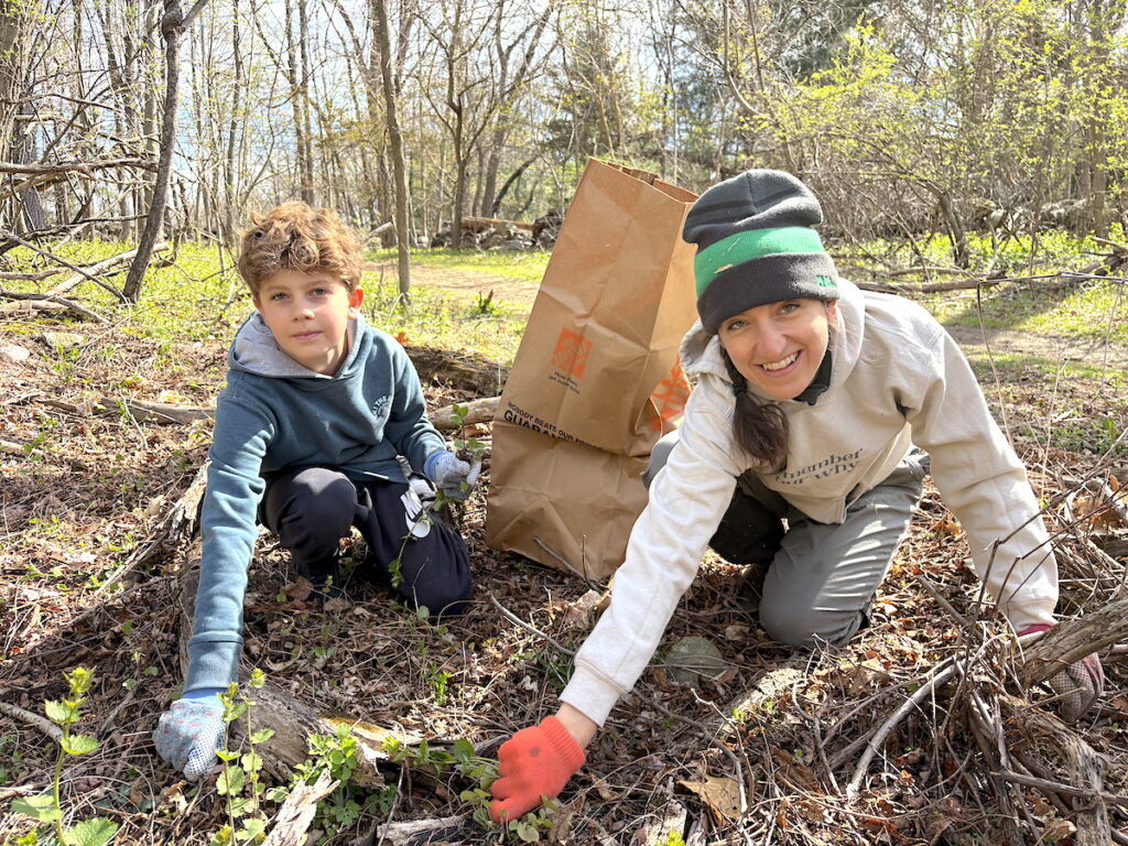A Mother and child kneel on the ground to remove invasive plants from Lone Tree Hill 